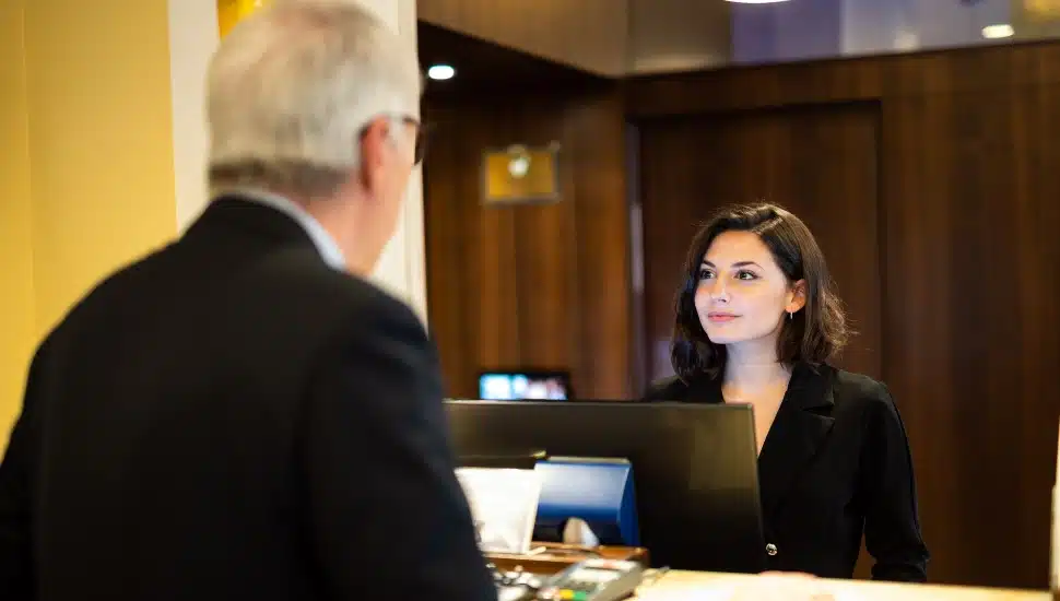 Young woman helps a businessman at a hotel reception desk, both smiling in a modern, elegant lobby.