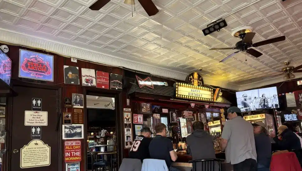 Interior of Ray's Happy Birthday Bar in South Philadelphia, showing the illuminated "Happy Birthday" marquee above the bar, tin ceiling, wood-paneled walls covered in memorabilia and neon beer signs, and patrons seated at the bar.