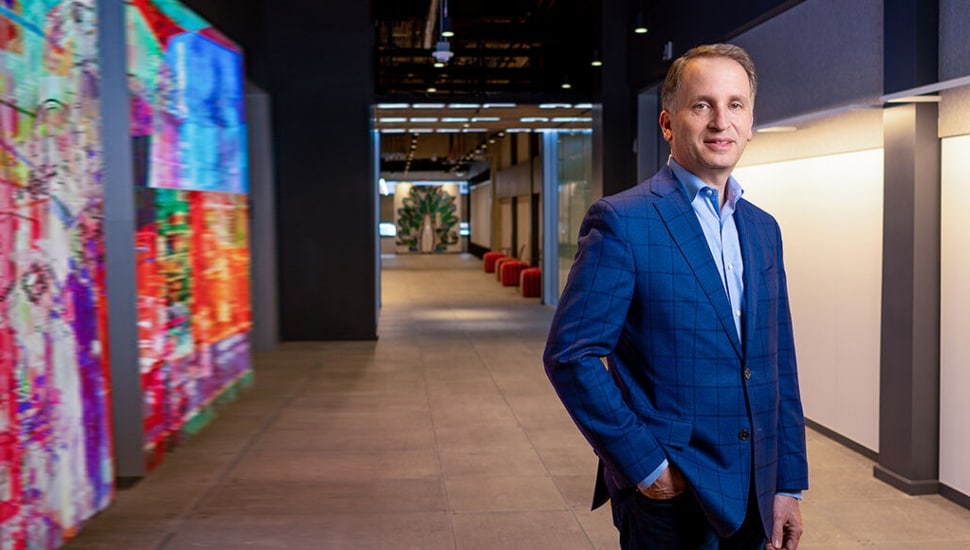 Sam Schwartz, Comcast executive, standing in a modern office corridor with colorful digital art displays at Comcast's Philadelphia headquarters.