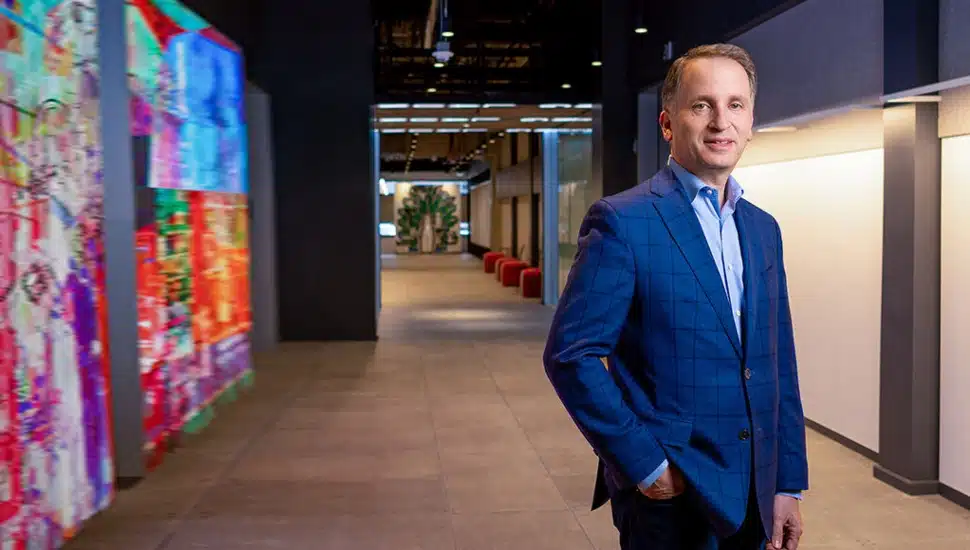 Sam Schwartz, Comcast executive, standing in a modern office corridor with colorful digital art displays at Comcast's Philadelphia headquarters.