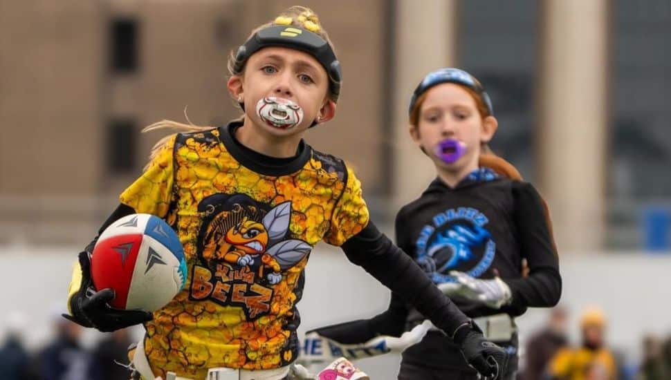 Young girls wearing uniforms and mouthguards playing flag football.