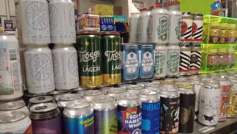 Rows of international beer cans displayed on a store counter, including Tröegs Lager, Free Will Cloudy, Green State, and Sunday Beer, among others.