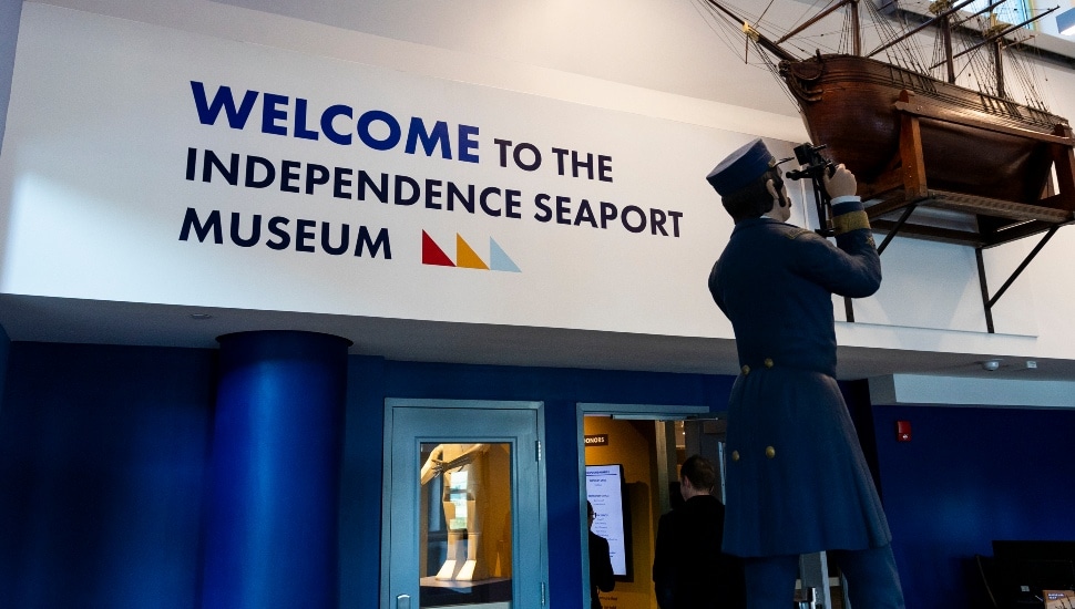 Lobby of Independence Seaport Museum featuring a "Welcome" wall sign and a uniformed sailor statue looking through binoculars.