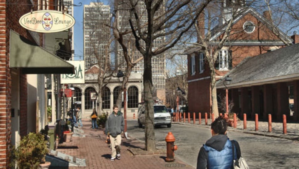Pedestrians walk a brick sidewalk past colonial-era buildings and modern high-rises in Philadelphia's Society Hill.