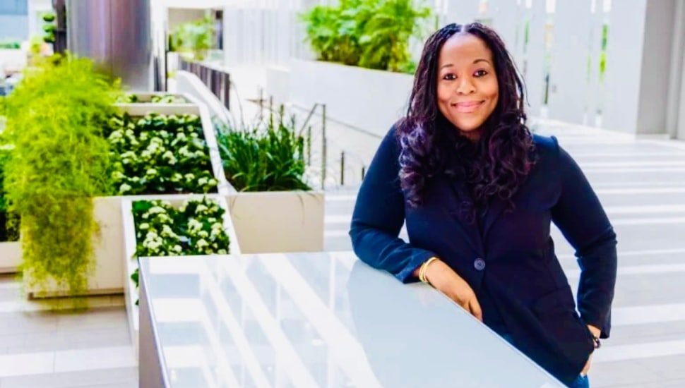 WealthMore founder and CEO Mical Jeanlys-White poses in a modern atrium surrounded by greenery.