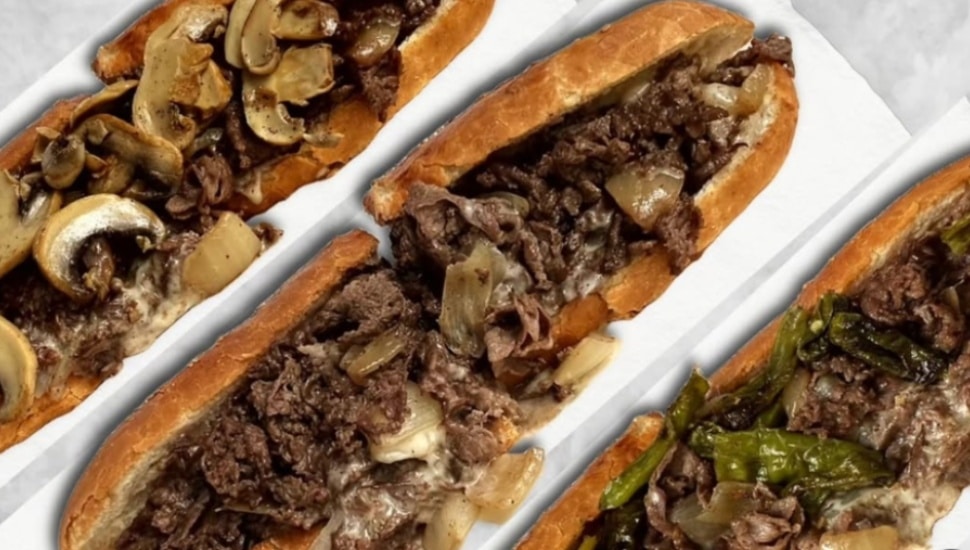 Three Wiir Philadelphia cheesesteaks on a white tray, topped with mushrooms, sautéed onions, and roasted peppers on seeded hoagie rolls.