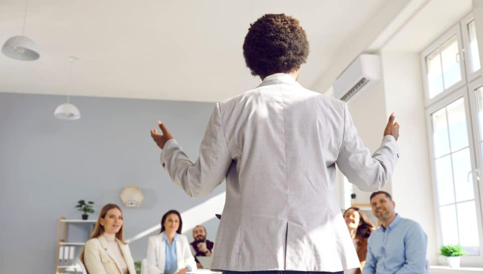 Woman of color presents to table of coworkers.